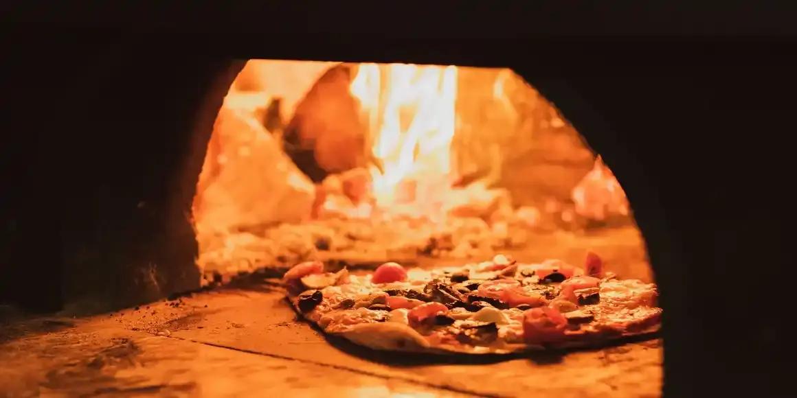 Pizza sliding into a wood-fired oven on a peel